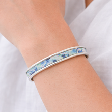 Silver bracelet with blue and green pattern on a wrist against a white background