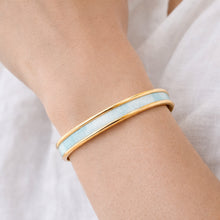 Gold and light blue bangle on a wrist against a white background