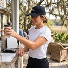 Woman in a white t-shirt and black cap buying coffee at an outdoor cafe.