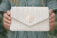 White knitted purse with a shell charm held by a person wearing a striped shirt.
