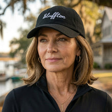 Woman wearing a black cap with 'Bluffton' text outdoors.