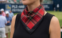 Person wearing a black sleeveless top with a red plaid scarf around their neck, standing on a sports field.