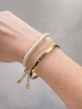 Close-up of a wrist wearing multiple gold bracelets on a neutral background nautical classic