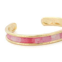 Gold cuff bracelet with pink plaid pattern on a white background