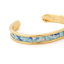 Gold bracelet with a blue floral pattern on a white background
