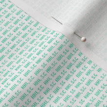 Close-up of fabric with green text pattern and pins on a white background