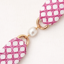 Earring with pink and white patterned strap and pearl accent on a light background