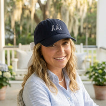 Woman wearing a navy cap with 'hii' on it, sitting outdoors.