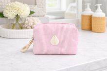 Pink toiletry bag on a bathroom counter with flowers and bottles in the background