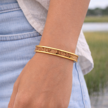 Gold bracelet on a wrist with a blurred natural background