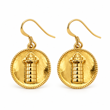 A pair of gold drop earrings featuring a circular medallion with a small lighthouse figure in the center, suspended from matching gold fishhook wires on a plain white background. Harbour town lighthouse coin earrings