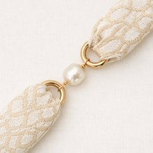 Close-up of a decorative ribbon with gold loops and a pearl on a light background