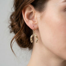 Gold horseshoe earring worn by a person with a neutral background
