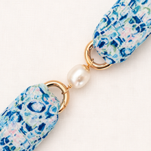 Close-up of a floral-patterned strap with gold rings and a pearl accent on a white background
