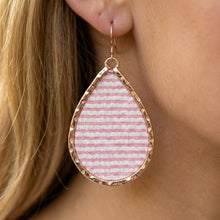Teardrop-shaped earring with pink striped design and gold frame worn by a person.