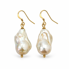 A pair of gold-tone drop earrings featuring irregular, baroque-shaped white freshwater pearls suspended from small gold beads, set against a plain white background.