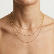 Close-up of a person wearing three gold necklaces on a neutral background