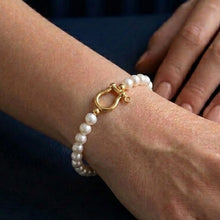 Pearl bracelet with gold clasp on a wrist against a dark background