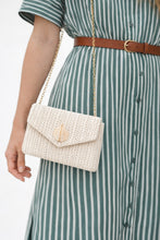 Person wearing a green and white striped dress with a beige woven handbag.