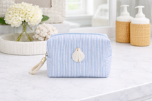 Blue striped toiletry bag with a shell charm on a bathroom counter.