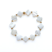 A beaded stretch bracelet featuring white mother-of-pearl clover-shaped beads and small gold spacer beads, arranged in a circle on a white background.