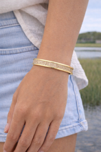Gold bracelet on a wrist with a blurred natural background