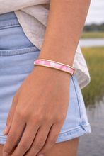 Person wearing a pink and gold bracelet by a body of water