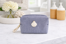 Navy striped toiletry bag with a shell charm on a bathroom counter.