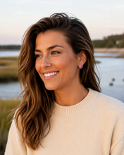 Woman with long brown hair wearing a beige sweater by a body of water.