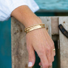 Hand wearing two gold bracelets with a blurred background