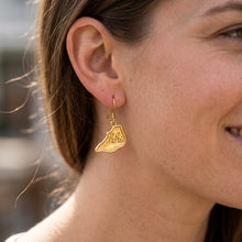 Close-up of a gold-tone hhi island dangle earring worn on an ear.