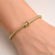 Gold bracelet with a knot design on a wrist against a neutral background