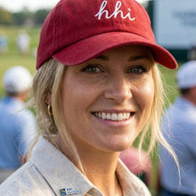 Woman wearing a red cap with 'hhi' on a golf course