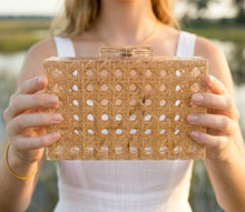 Person holding a woven clutch bag outdoors with a blurred natural background