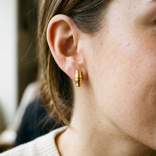 A close-up of a person's ear wearing a small gold hoop earring with a textured, segmented design.