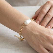 Gold bracelet with a pearl on a wrist against a neutral background