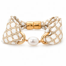 A gold-tone bracelet featuring a patterned white and beige fabric band, a central white pearl, and gold-tone metal rings, shown on a plain white background.