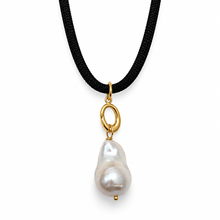 A black cord necklace featuring a gold-tone oval ring connector and a large, irregular white baroque pearl pendant, shown against a plain white background.