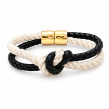 A double-strand braided rope bracelet featuring one black braided cord and one cream/off-white braided cord, tied in a knot at the center, finished with a polished gold magnetic clasp on a white background.