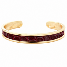 A gold-plated cuff bracelet featuring a central inlay of dark red crocodile-embossed leather, shown against a plain white background.