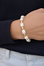 Pearl and gold bracelet on a wrist with a dark ribbed sweater and light blue jeans.