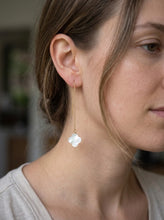 Model wearing a long fine-chain earring ending in a small white clover.