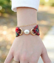 Bracelet with plaid design and pearl-like bead on a wrist against a blurred natural background