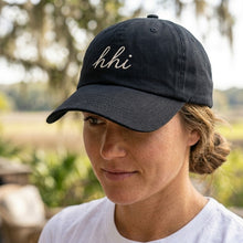Person wearing a black cap with 'hhi' text outdoors