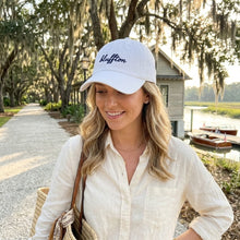 Woman wearing a white cap with 'Bluffton' text, standing outdoors near a body of water.