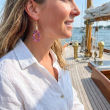 Woman on a boat wearing a white shirt and colorful earrings, with water and sky in the background.