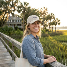 Woman wearing a cap and holding a tote bag on a wooden bridge with a scenic background
