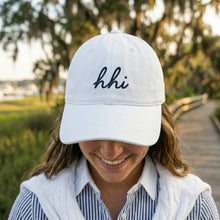 Person wearing a white cap with 'hhi' text outdoors