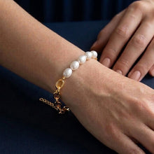 Pearl bracelet with a gold chain on a wrist against a dark background