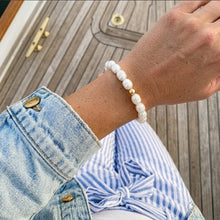Hand wearing a pearl bracelet with denim jacket and striped shirt on wooden surface